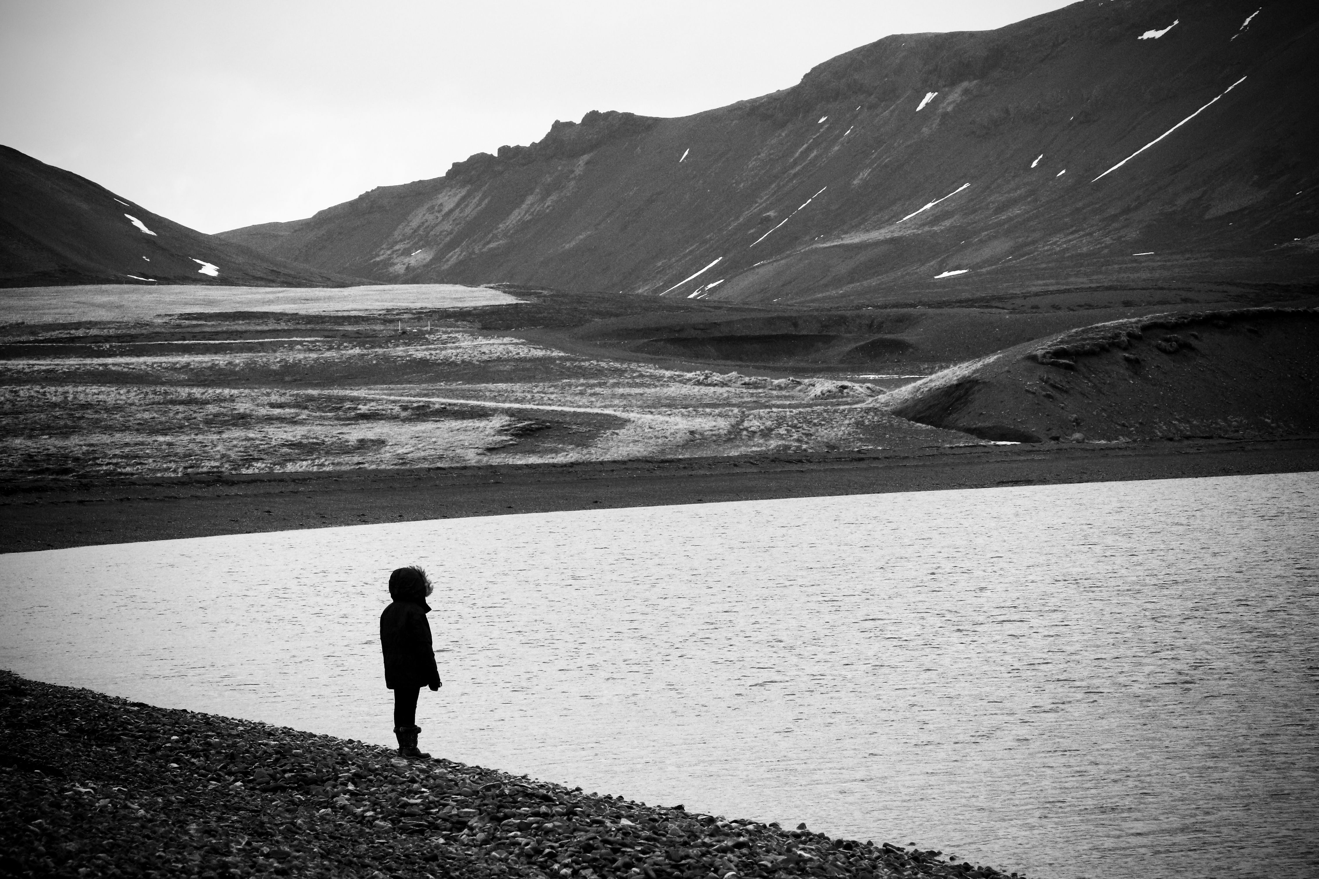 Black and white photo of lone child silhoutte against a backdrop of bay and mountains. The atmosphere is a bit bleak and lonely. Taken in Iceland. 
