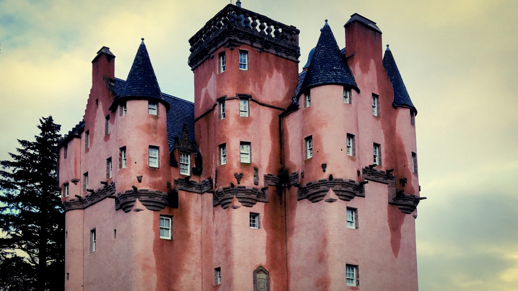 Photo of the upper storeys of a very pink scottish castle. It's all wee turrets and small windows and pink. 