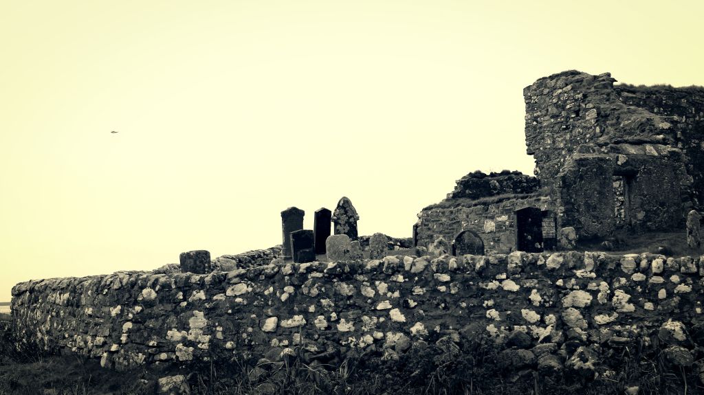 sepia tinted photo of a ruined chapel and old gravestones behind a low stone wall, taken on North Uist. 